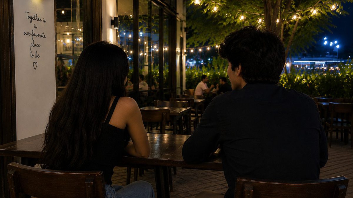Two people sitting side by side and talking at an outdoor café table in the evening